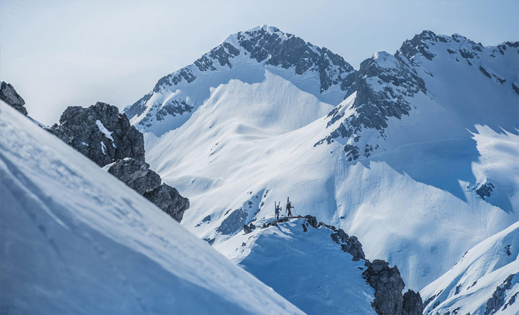 Twee freeriders lopen op met sneeuw bedekte bergen.