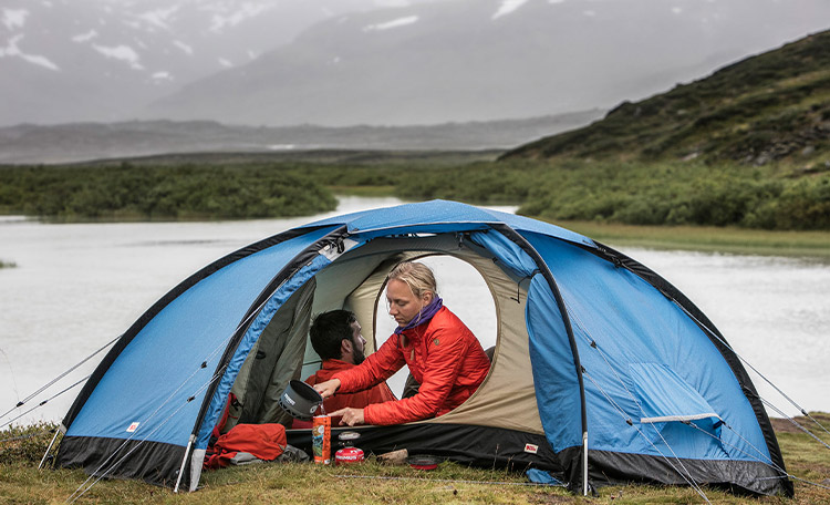 Vrouw en man zitten in een tent voor een meer